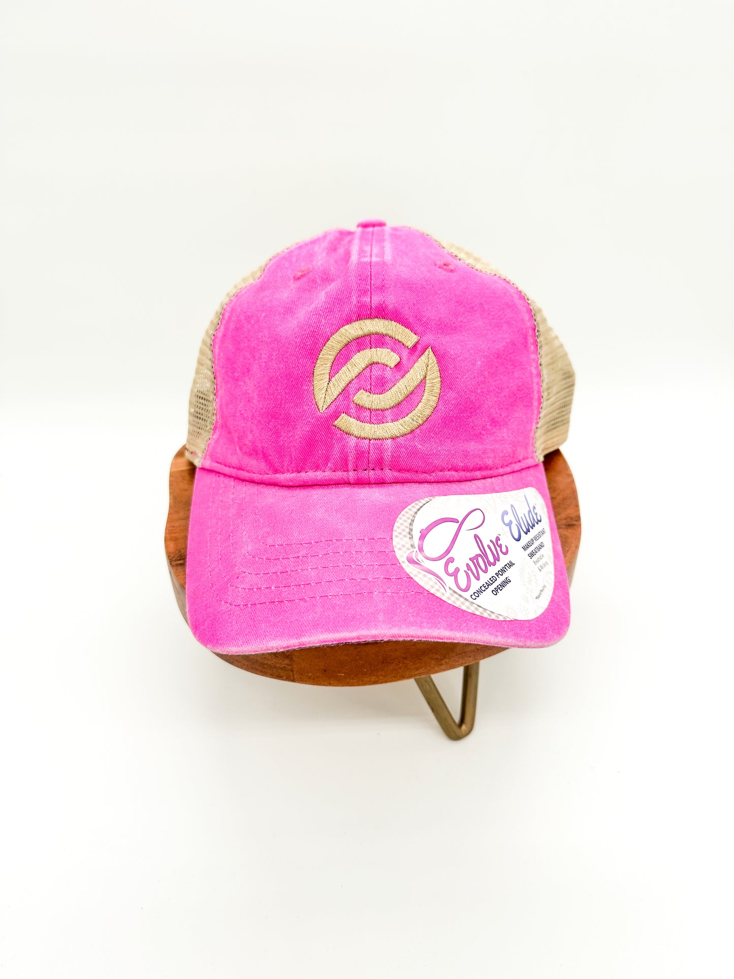 A pink trucker cap with a logo in gold thread on the front, displayed on a mannequin head.