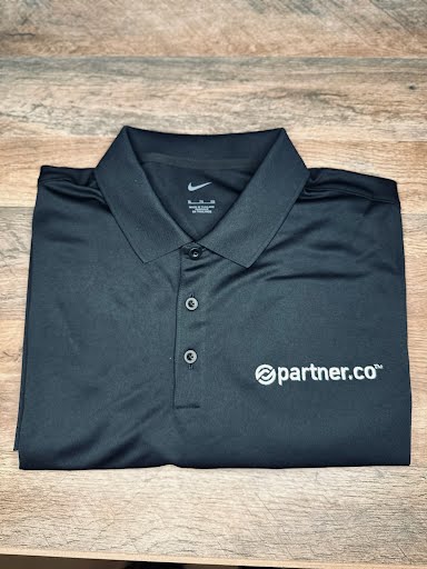 A black Nike Dri-FIT polo shirt with an embroidered white PartnerCo logo, featuring a flat knit collar, a three-button placket, and open hem sleeves.