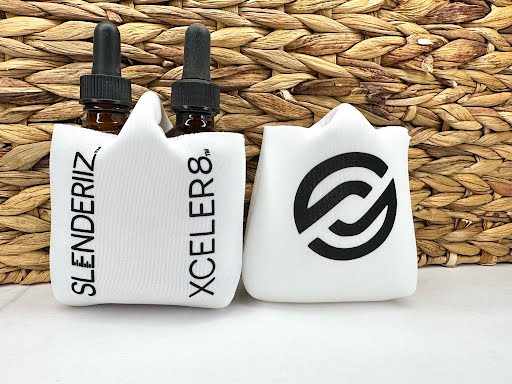 Two skinny drops bottle holders with printed designs, one in white with a green design and the other in white with a black design, displayed against a woven background.