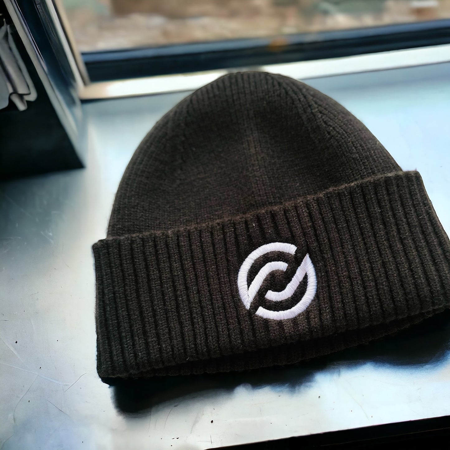 A black beanie with an adjustable cuff, featuring a white logo on the fold.