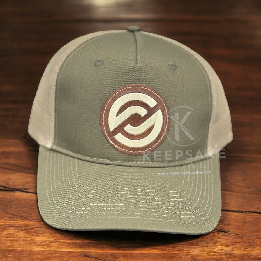An olive green and beige trucker cap with a tan embroidered design on the front.