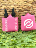 Two pink bottle holders with logos and text 'SLENDERIZ. XCELER8.' displayed on them, placed on a green leafy surface.