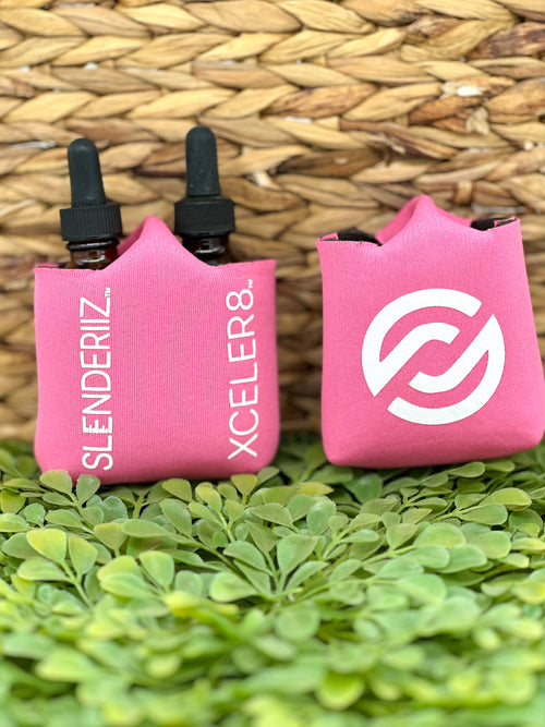 Two pink bottle holders with logos and text 'SLENDERIZ. XCELER8.' displayed on them, placed on a green leafy surface.