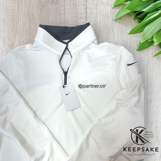 White Nike jacket with a visible brand tag on a wooden surface with green leaves.