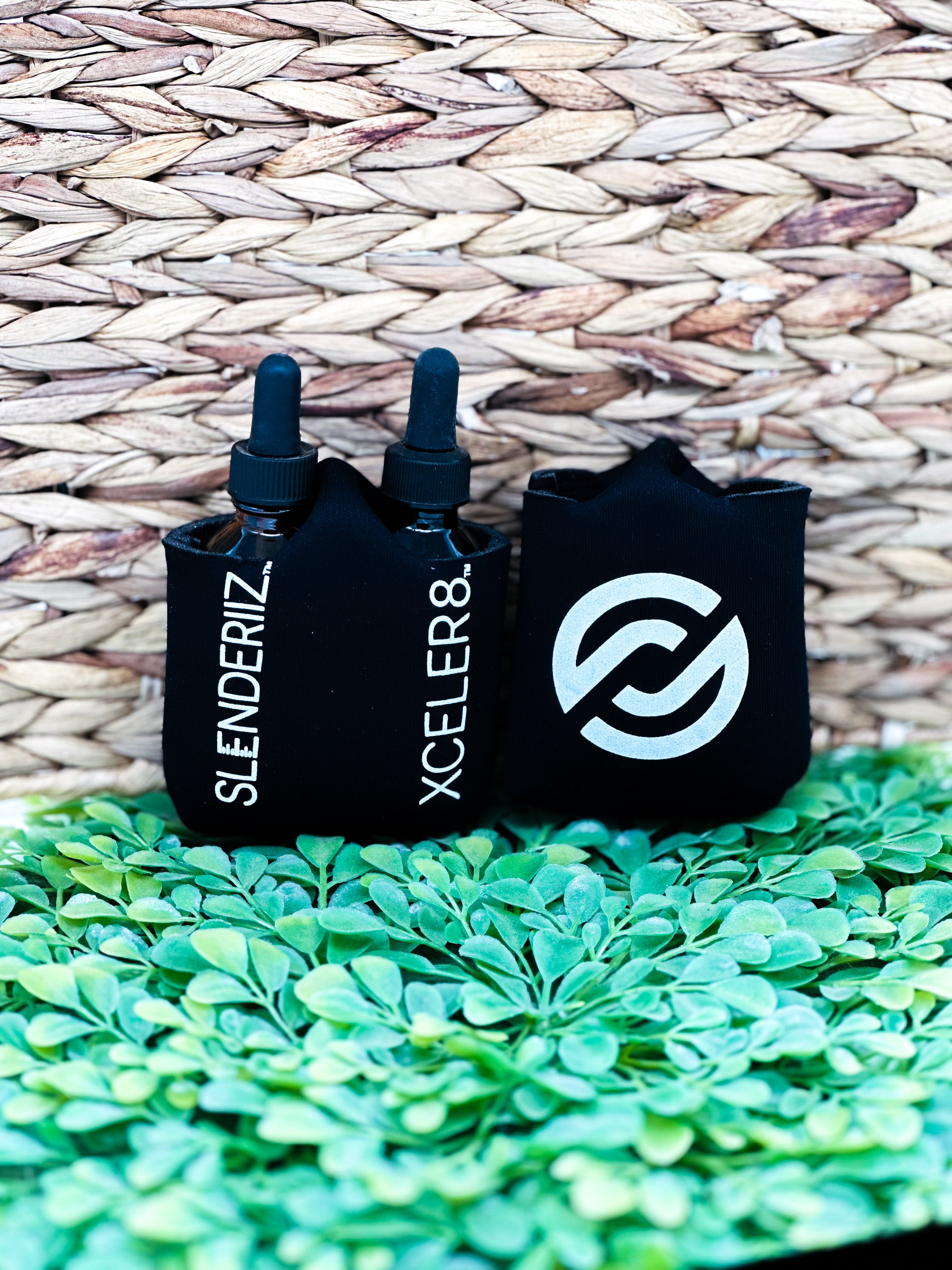 A pack of 10 black bottle holders for Skinny Drops displayed on a green surface with a woven basket background. The holders have white text and logo.