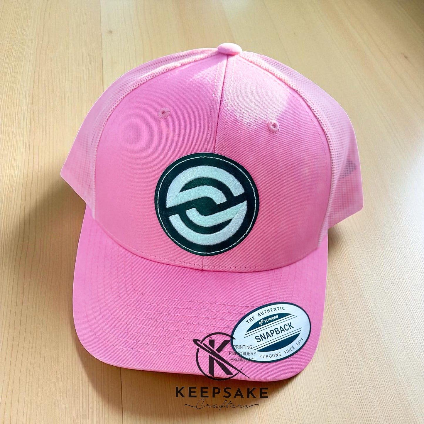 Pink cap with a black logo on a wooden stump outdoors Pink Snapback Cap | Partnerco Swag